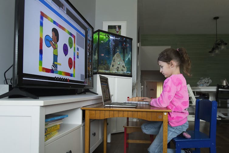 Coronavirus outbreaks are inevitable if Ontario reopens schools 15 A young girl in a pink sweatshirt sits in front of a laptop and a bigger computer monitor displaying lessons.