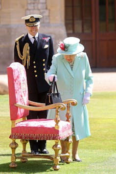 엘리자베스 2세 여왕이 핸드백을 의자 위에 놓고 윈저 성에서 열린 행사에서 토마스 무어 대위에게 기사 작위를 수여하고 있습니다.