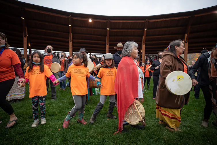 Young people in orange T-shirts dancing with people with drums in a circle.