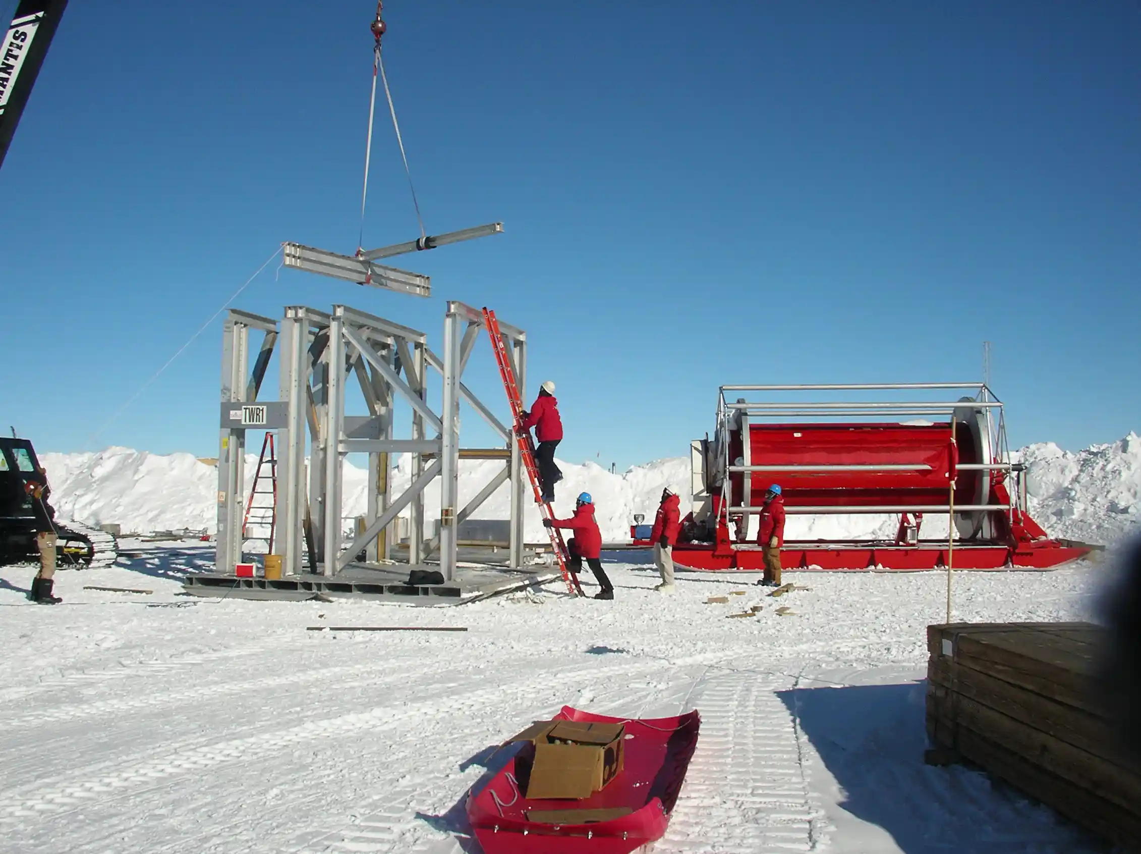 Bundled up construction workers with metal beams on snowy landscape.