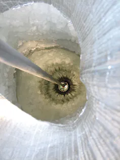 A tether descends into a vertical tunnel through snowy ice.