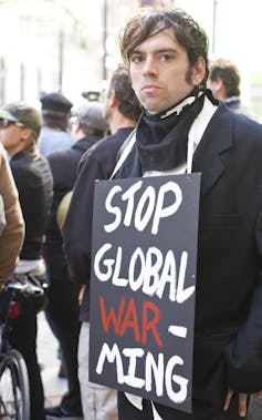 A man looking at the camera with a sign around his neck reading 'Stop Global Warming'