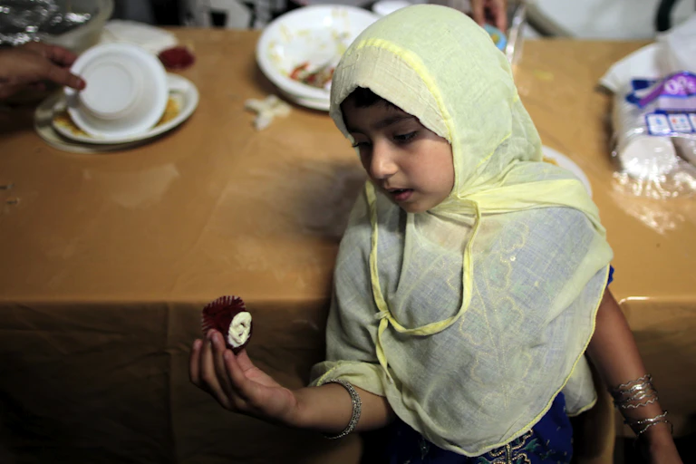 A young girl, with her head covered, sitting on a chair.