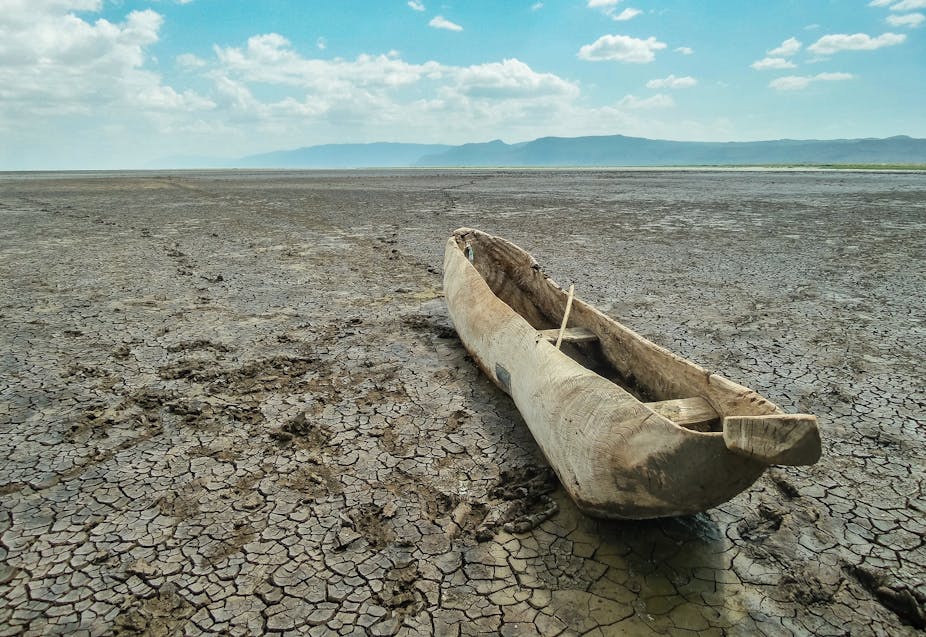A wooden canoe lies on parched ground.