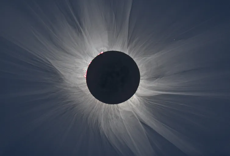black circle of the Moon outlined by white rays against a dark sky