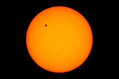 Orange orb of the Sun with a small black dot visible against it