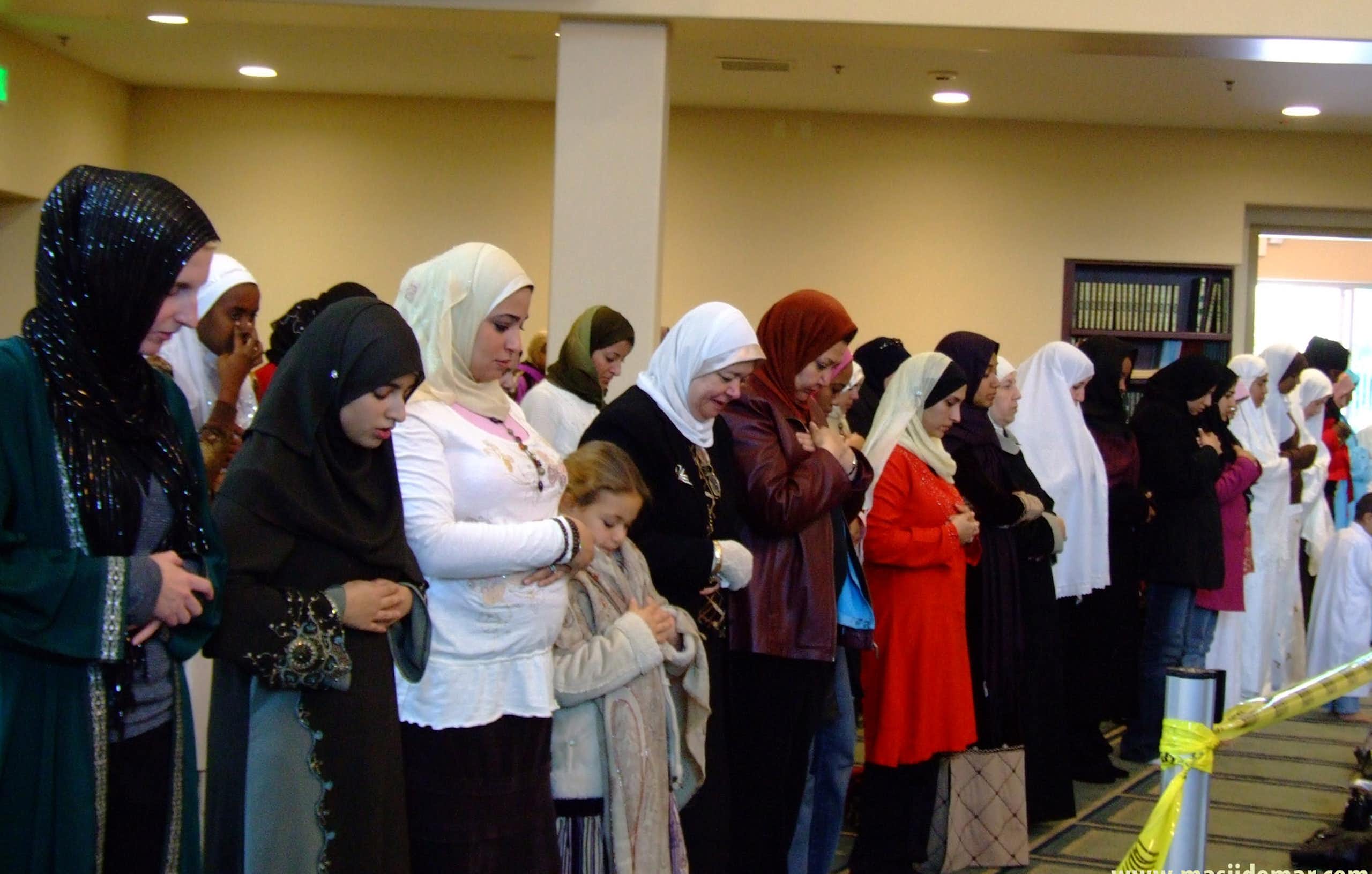 Women wearing headdresses praying with their heads bowed.