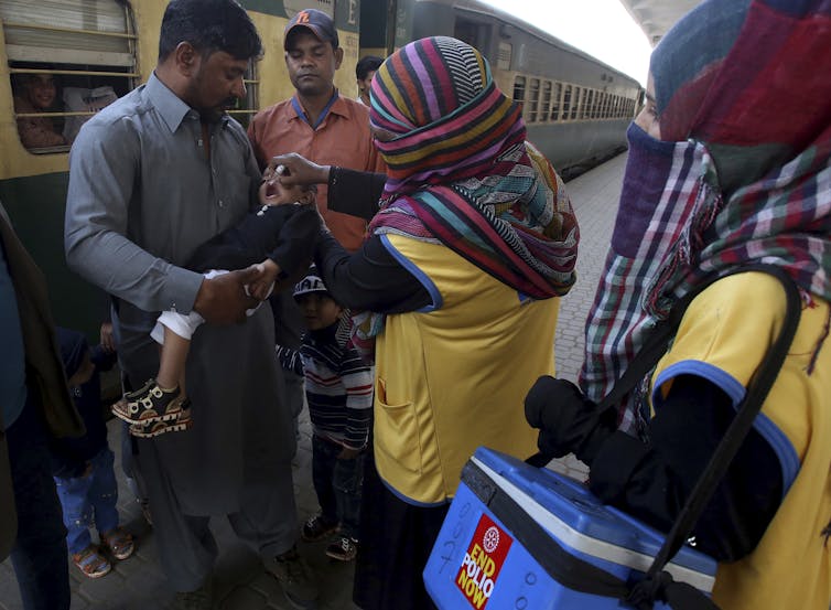 A health worker gives a polio vaccine to a child at a railway station in Pakistan. AP Photo/Fareed Khan