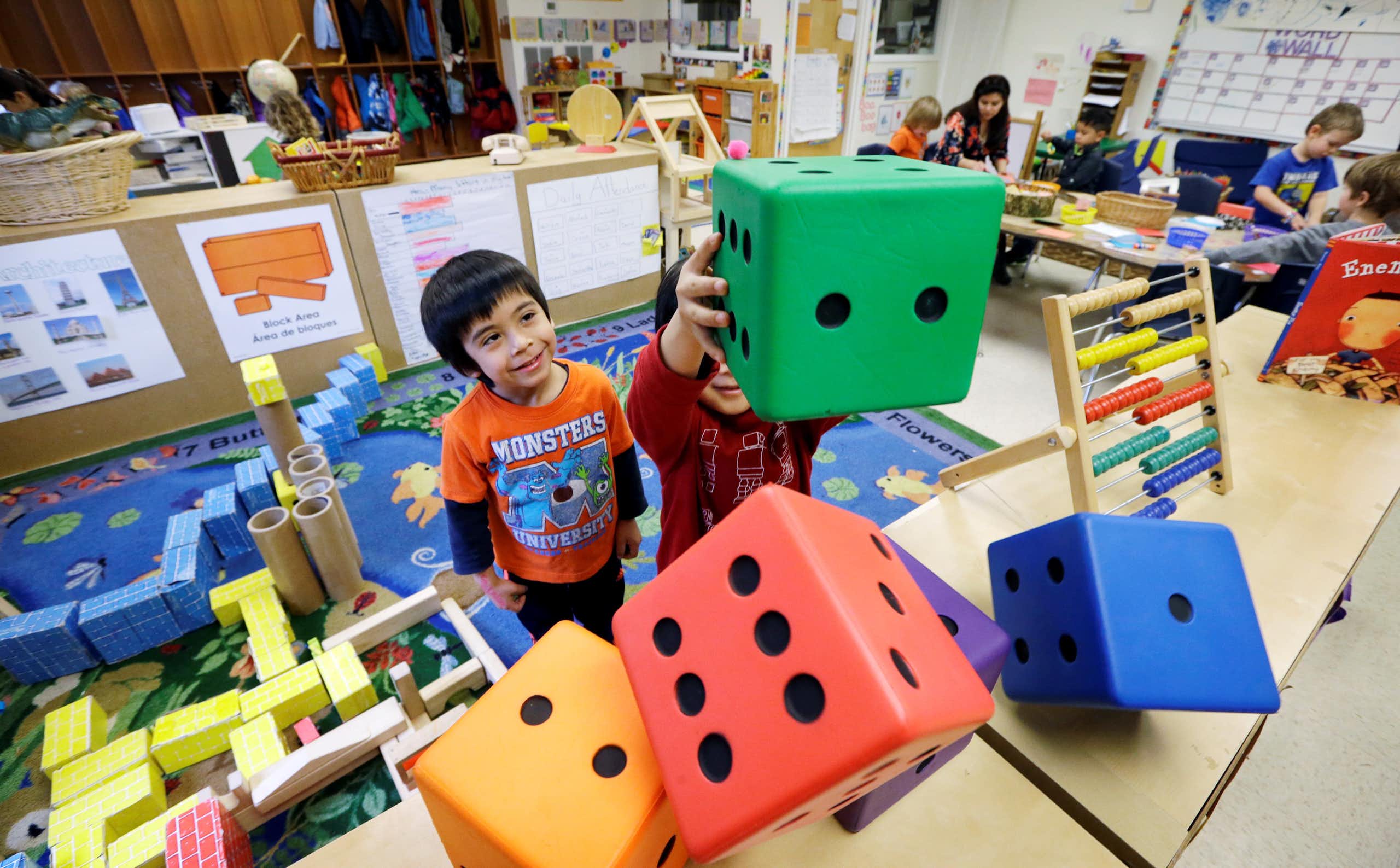 Young children play with giant, multicolored dice in a classroom.