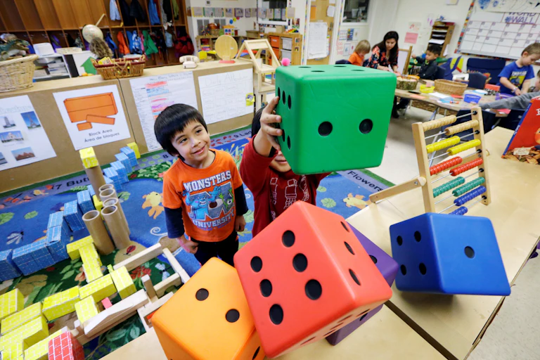Young children play with giant, multicolored dice in a classroom.
