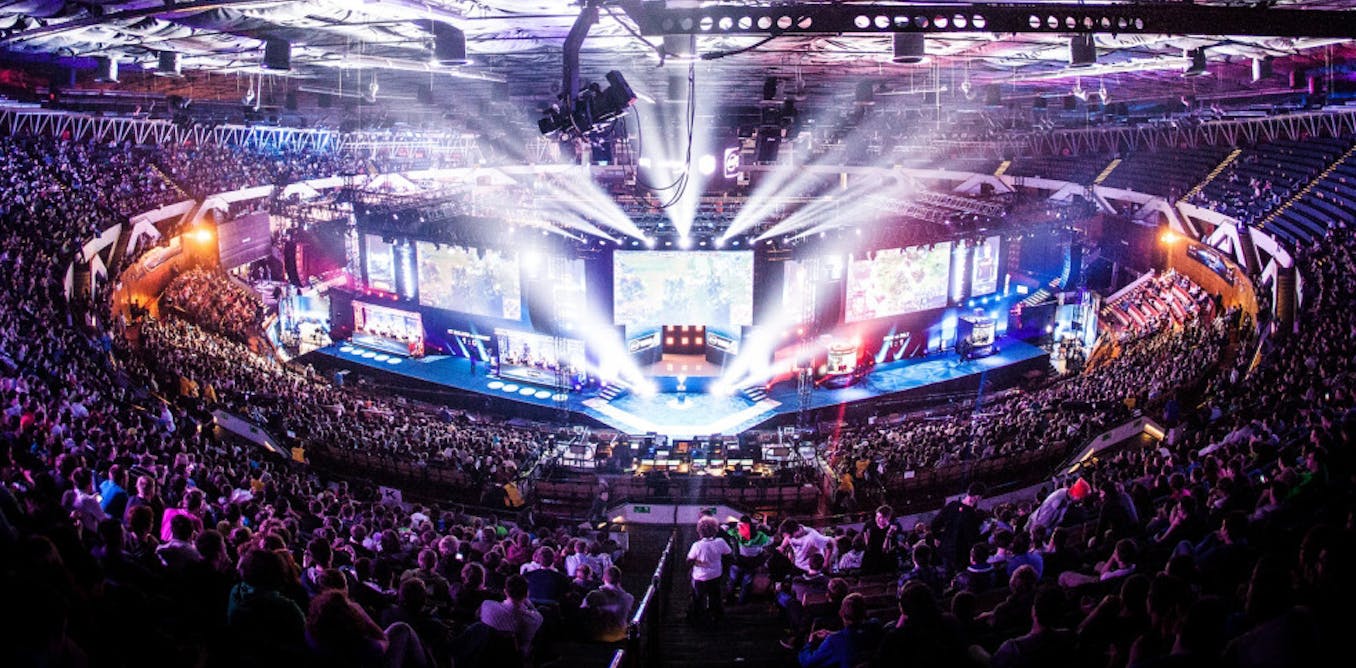 Scène et public d'un tournoi d'eSport, vus d'en haut. La salle semble fortement remplie.