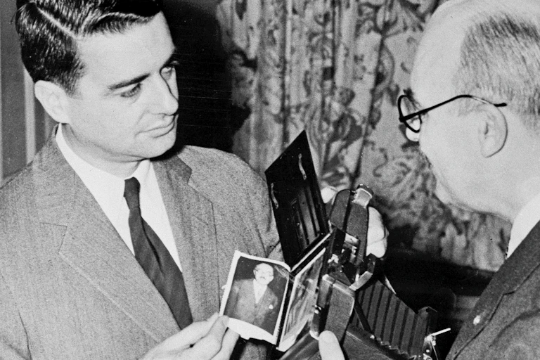 two men look at each other over a camera with an instant photo