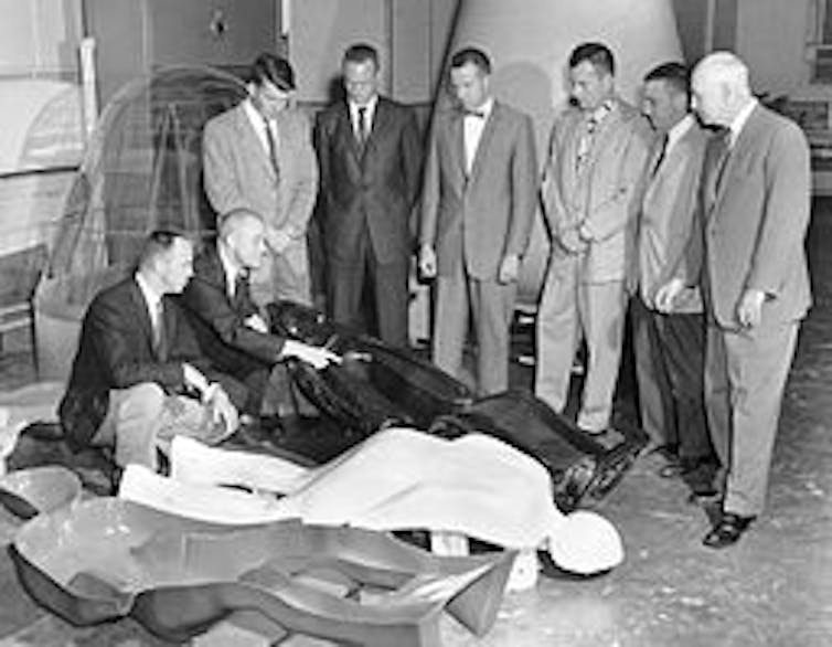 Mercury 7 astronauts, including John Glenn, second from left, examine what NASA called their ‘couches,’ or their seats that had been molded to fit plaster casts of their bodies.