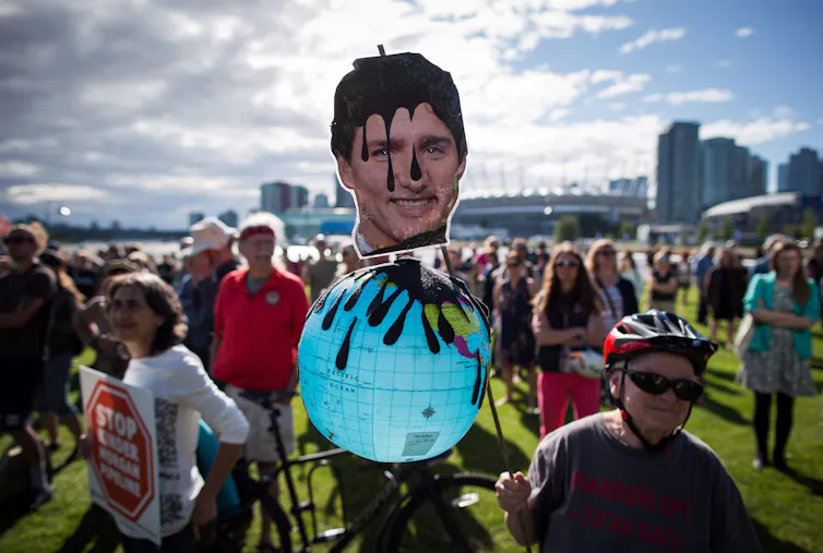 A protester holds a sign that shows justin trudeau's head soaked in oil