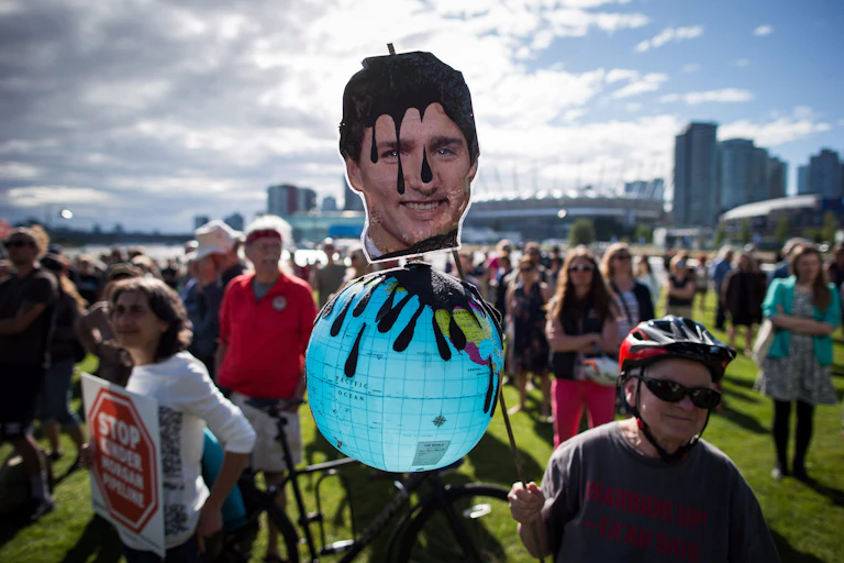 A protester holds a sign that shows justin trudeau's head soaked in oil