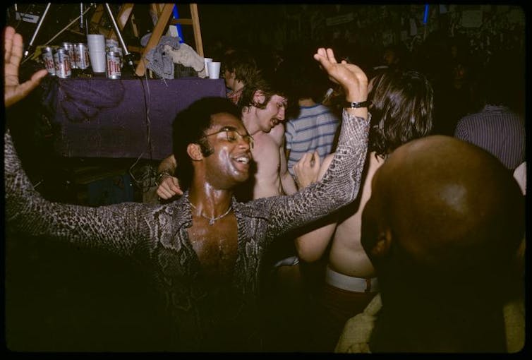 A dance at Gay Activist Alliance Firehouse in 1971, man raises his hands, smiling and dancing