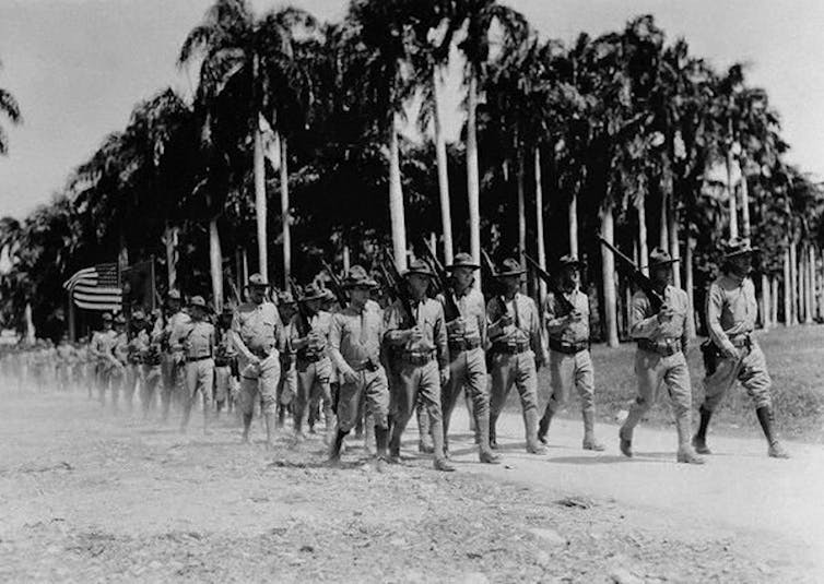 Marines march with palm trees in the background.