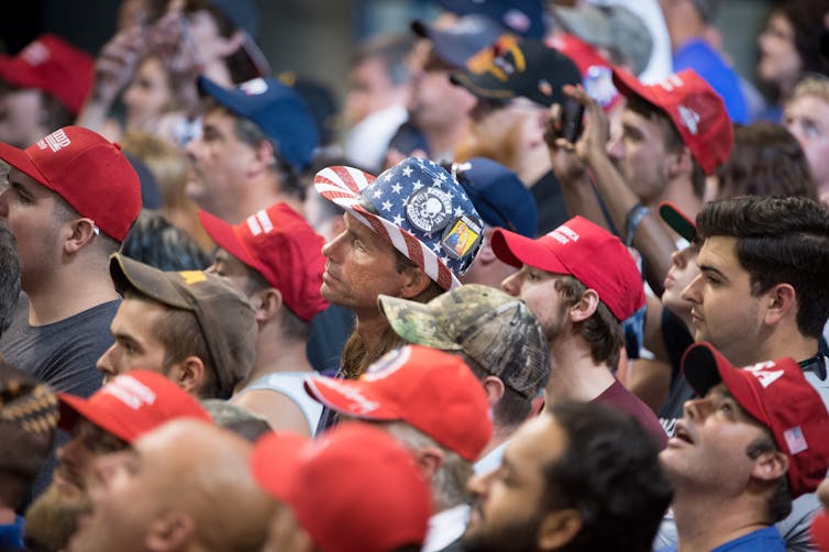 A group of people, the majority of whom are wearing red Make America Great Again baseball caps