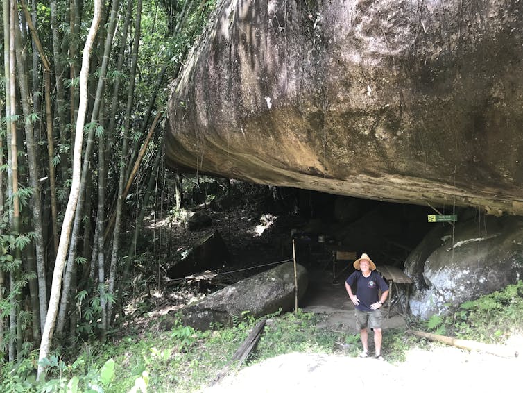 man stands beneath a big rock overhang