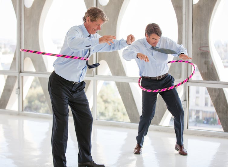 Two men in office attire using hula hoops