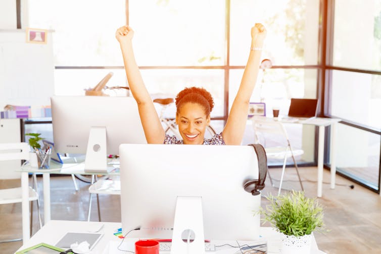 Smiling woman raising her hands in front of a computer
