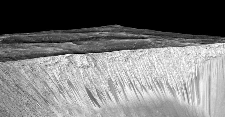 Los científicos sostienen la hipótesis de que las vetas estrechas y oscuras fueron formadas por agua líquida salada -necesaria para la vida- que fluye por las paredes de un cráter en Marte. Foto: NASA