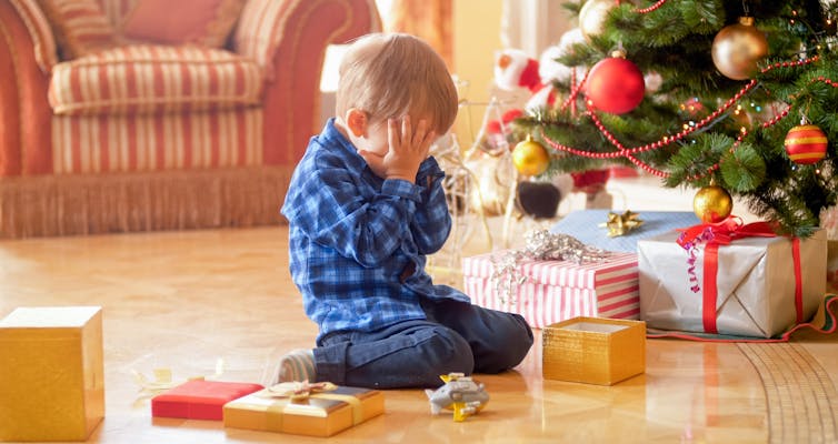 Child covering face by two hands in front of Christmas Tree 