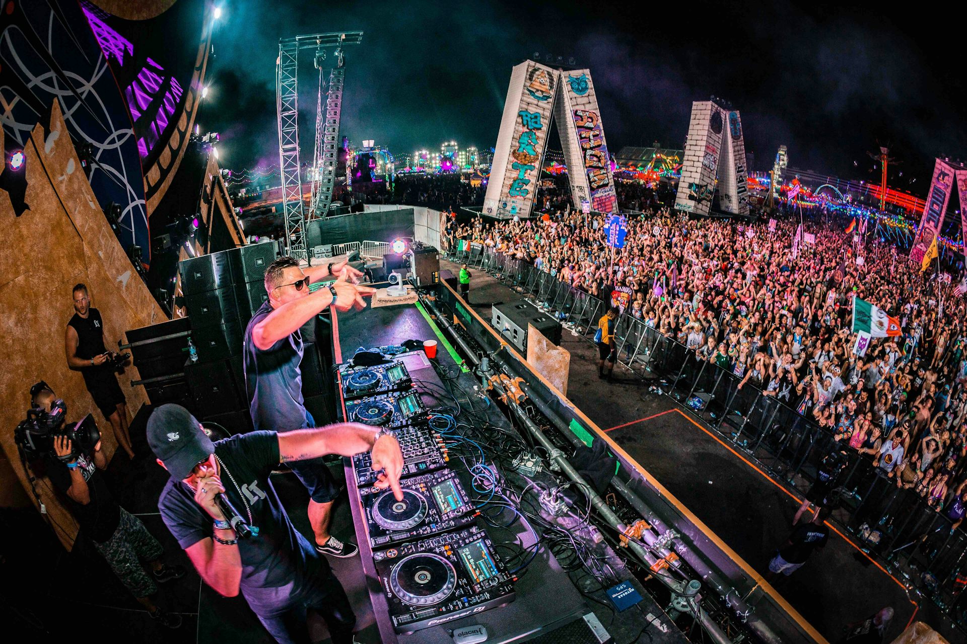 An aerial view of two DJs performing in front of a large crowd at a festival