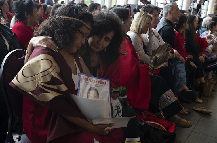 Two women sitting in the audience sadly embrace during the MMIWG report ceremonies.