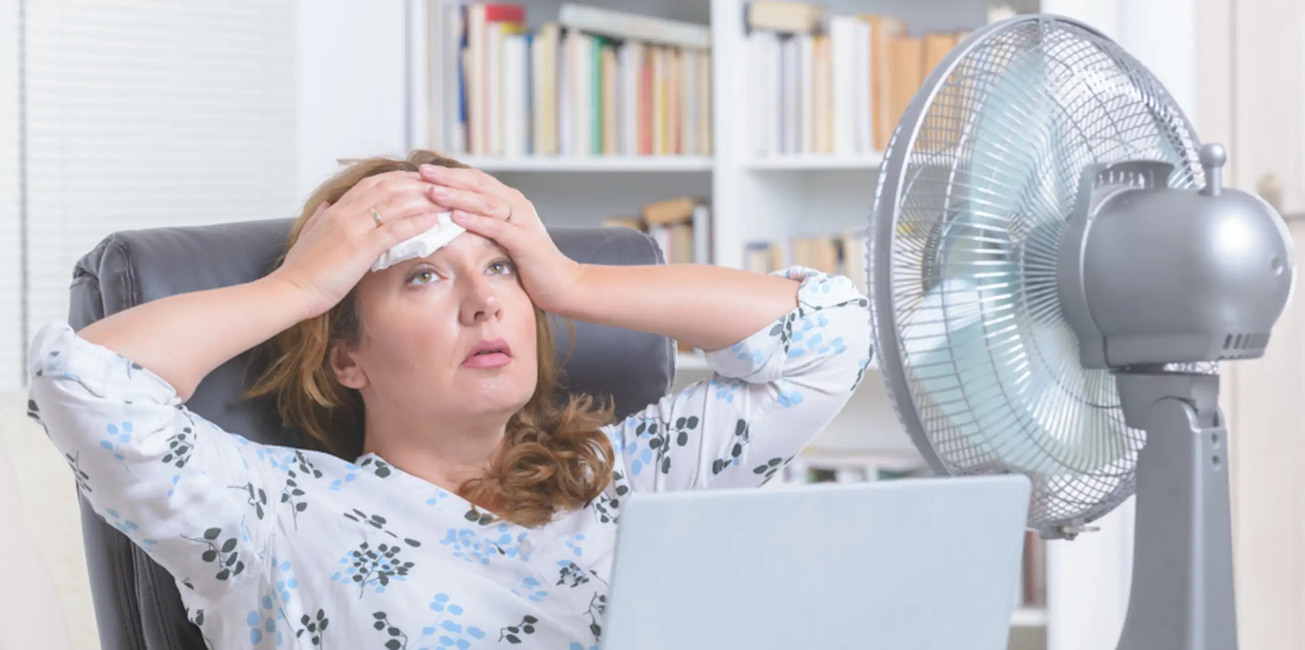 Une femme écrasée de chaleur, face à un ventilateur.