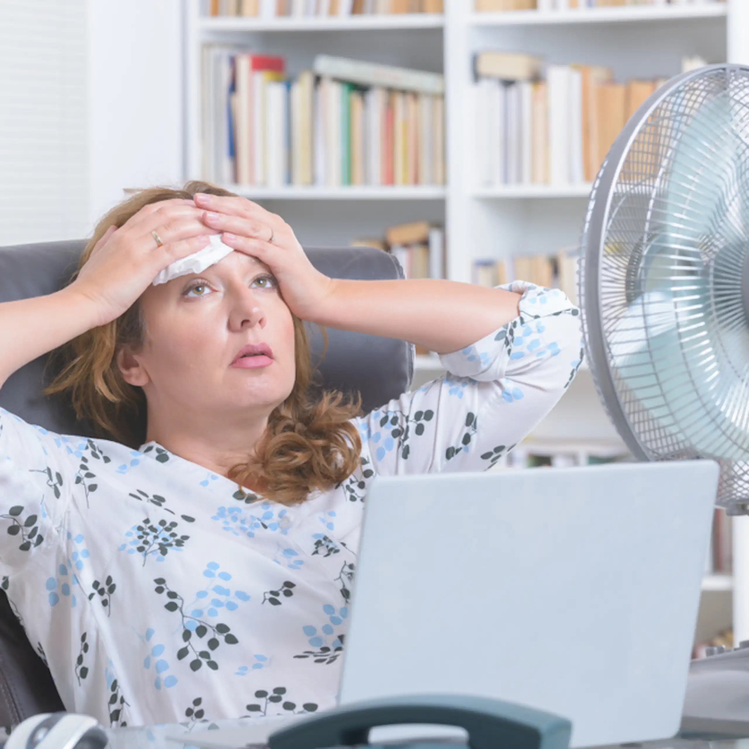 Une femme écrasée de chaleur, face à un ventilateur.