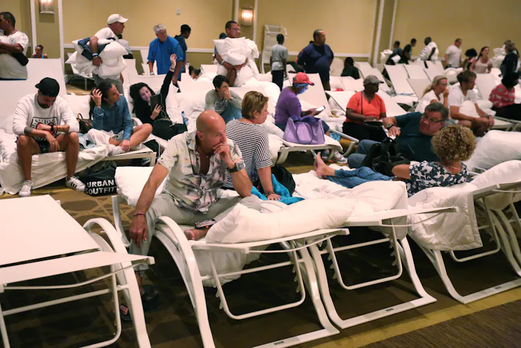 a mix of people wearing street clothes sit on beach chairs