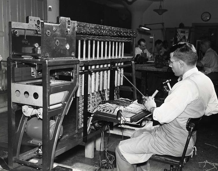 A census card counter with glasses using a machine while sitting in a chair in a black and white photo