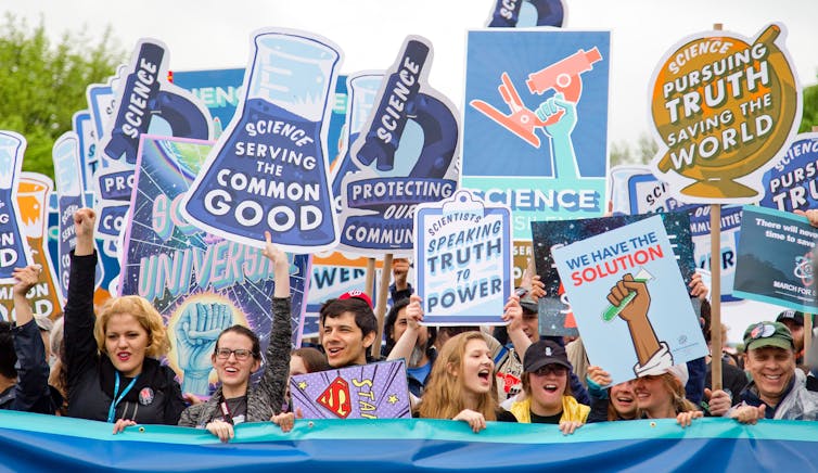 Adults holding up signs about the power of science behind a blue banner