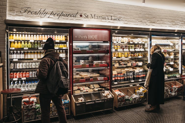 A wall of PRET with two customers looking at food and drink