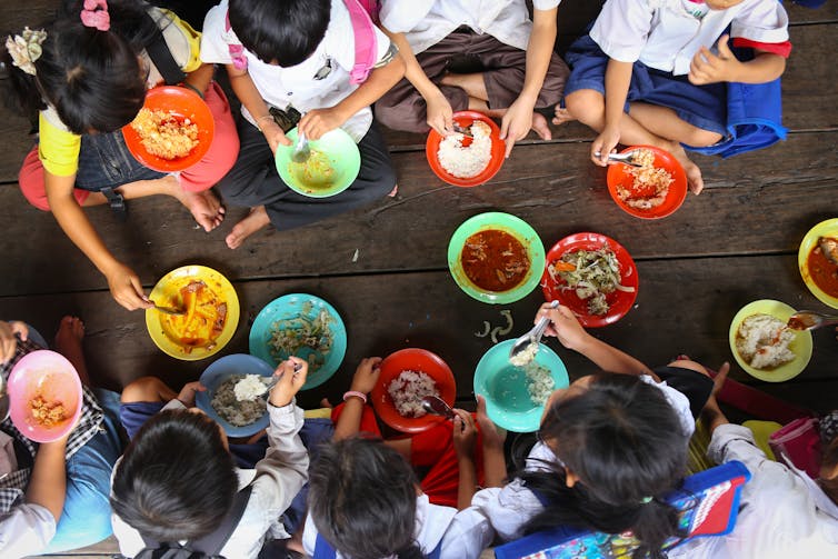 Children sat on floor eating food from coloured bowls