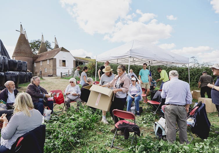 UK hop picking trip - crowd of adults around boxes and chairs in a garden