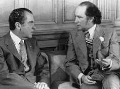 a black and white photo of two men talking, both with thinning hair