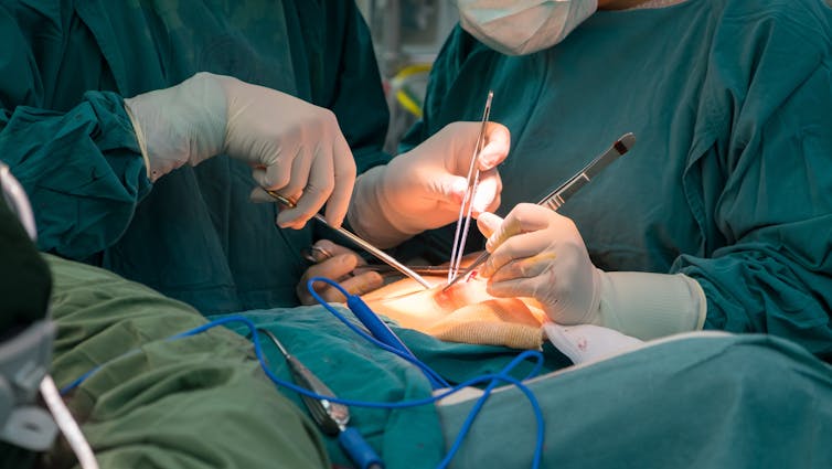 Stock photo, closeup of surgery. No blood, just bright lights, hands holding scalpels