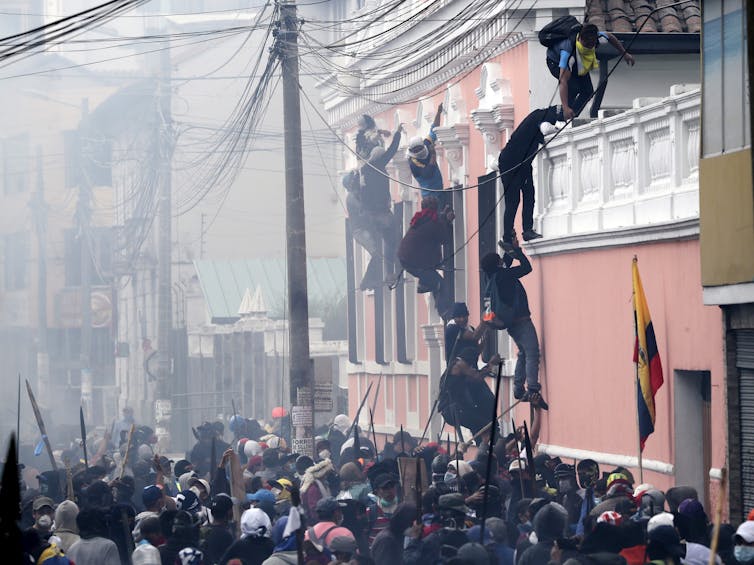 Manifestantes antigubernamentales escalan la fachada de una residencia en busca de una mejor posición para enfrentarse a la policía en Quito (Ecuador), en octubre de 2019. (AP Photo/Dolores Ochoa)