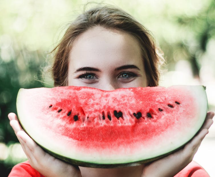 Woman smiling holding a watermelon over her mouth