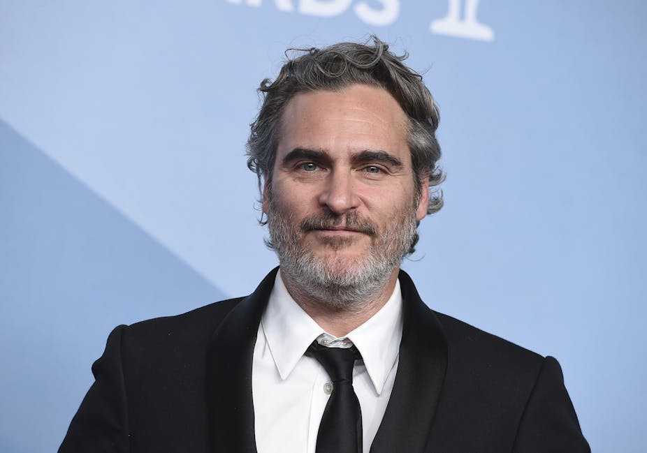 Close-up of Joaquin Phoenix wearing a tuxedo in front of a blue background
