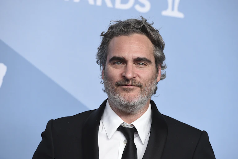 Close-up of Joaquin Phoenix wearing a tuxedo in front of a blue background