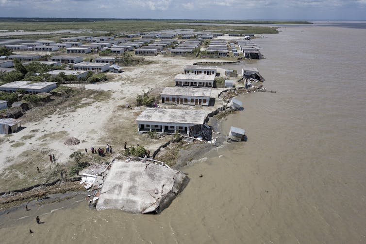 Several houses built along river bank, crumbling and breaking as river erodes the soil