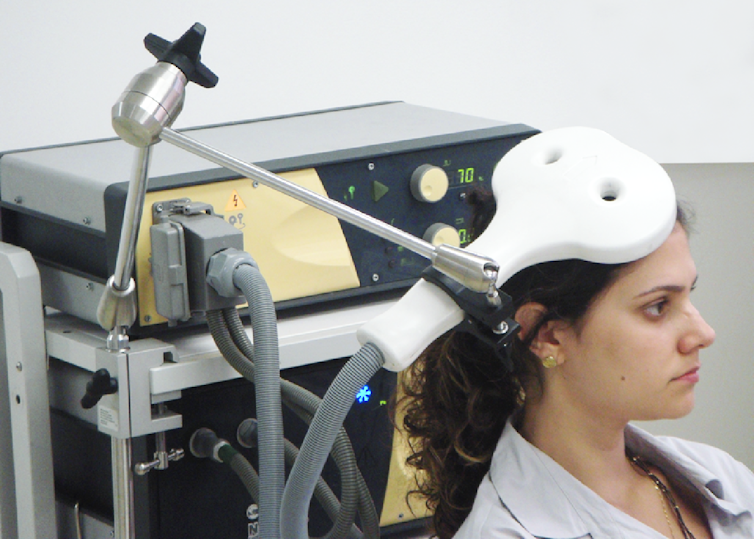 A woman is seated in front of a machine with an arm of the machine extended next to her head