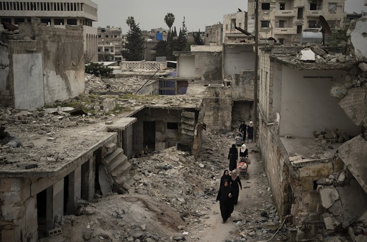 Women walk through rubble near a demolished building.