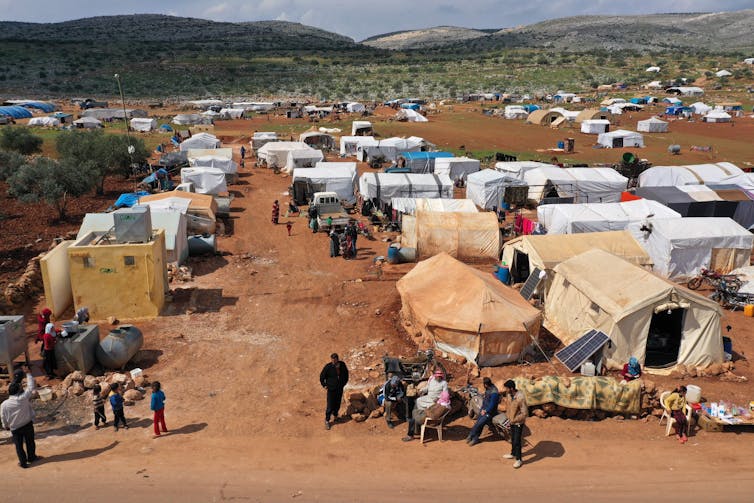 Dozens of tents are scattered across red sand, with mountains in the background.