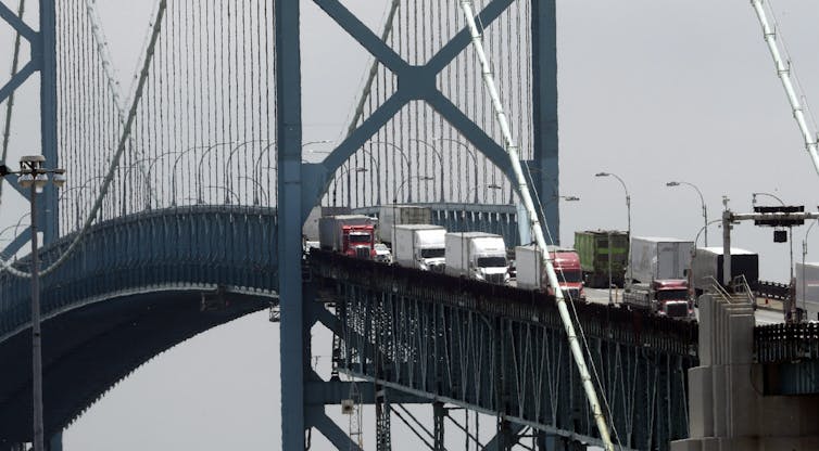 A large row of transport trucks travel across a bridge.