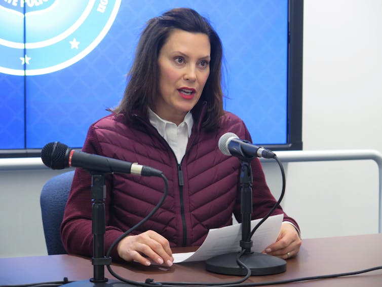 Gov. Gretchen Whitmer sitting in front of microphones, reading from a paper