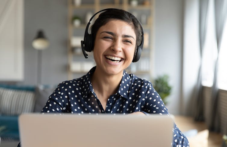 Girl wearing headphones, laughing, in front of a computer